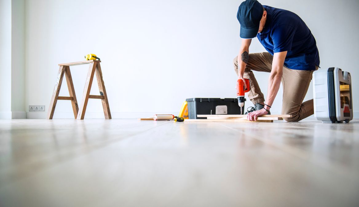 A handyman drilling a piece of wood on the floor